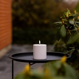 A round, white LED pillar candle for outdoor use, measuring 10 cm in diameter and height, suitable for creating a cozy ambiance in outdoor spaces.