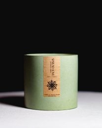 Concrete candle in a round, tall green container with a simple sun design on the side.