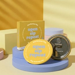 Yellow magnetic bottle opener with "open sip repeat" text, round shape, blue accents.