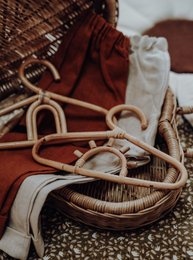 Set of 10 rattan hangers for kids' wardrobes, featuring a natural woven design with metal hooks for hanging clothes.