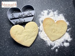 Heart-shaped baking decoration with two names engraved on it, made of light-colored dough or pastry.