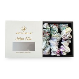 A set of iridescent garden silk scrunchies in white, green, and purple. The scrunchies have a soft, flowing texture and a delicate, floral-inspired design.