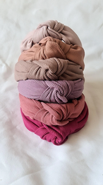 Ribbed knot headband in various shades of pink, including raspberry, dusty pink, clay pink, and fuchsia. Made of soft, stretchy material for a comfortable fit.