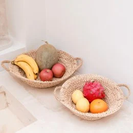 Woven raffia bowl with assorted fruits including apples, bananas, and citrus. Natural fiber basket for storing and displaying fresh produce.