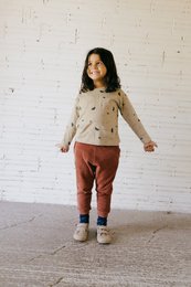 Long, loose-fitting terracotta-colored sweatpants with a beige long-sleeved top featuring a subtle print pattern. The outfit appears comfortable and casual, suitable for children.