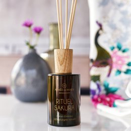Elegant reed diffuser with a wooden base and a floral fragrance. Features a dark glass bottle and natural rattan reeds.