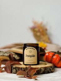 Autumn-themed candle with vanilla pumpkin scent, displayed on wooden slices with fall foliage.