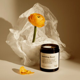 Tall, round, yellow candle with a single orange flower. Scented candle in a black glass container.