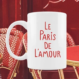 A white ceramic mug with the text "A LA VIE L'AMOUR" printed in red on the side. The mug is being held by a person wearing a plaid shirt, suggesting this is a decorative or novelty mug.