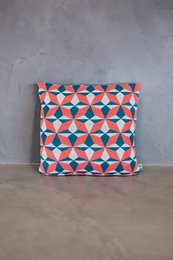 Cushion cover with a geometric pattern in shades of coral, blue, and white. Made of a soft, textured fabric.