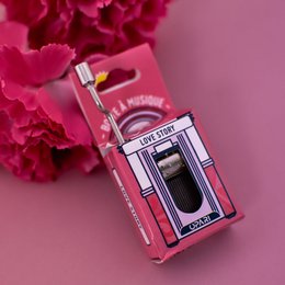 A pink and white music box with the text "Love Story" on the packaging. The music box appears to be a decorative item, possibly for a romantic occasion.