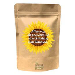 A round, tall yellow sunflower with the text "All that happens to you is a ... (sunflower)" on the product packaging. The sunflower is the focal point of the image, with a warm, natural color palette. The product appears to be a garden or home decor item.
