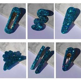  Glittery teal resin hair clips in various shapes and sizes, including a heart, crescent moon, and abstract designs.