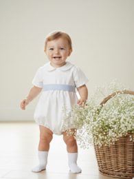 White baby romper with blue sash, suitable for formal occasions. Made of soft, breathable fabric. Available in sizes 0-3 months, 3-6 months, 6-9 months, and 12-18 months.