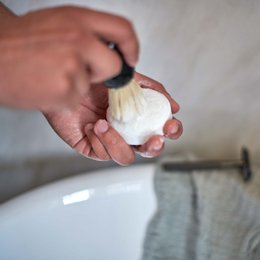A round, white shaving bar in a blue and yellow box labeled "POWER SHAVE SHAVING BAR 80 G / 2.82 OZ" for beard care.