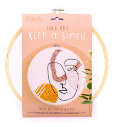 A round, wooden punch needle kit with a simple line art design featuring a face. The kit includes a wooden hoop and instructions for punch needle embroidery.