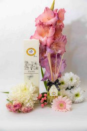  Floral reed diffuser with pink and purple flowers, glass bottle with white label and yellow logo.