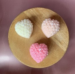 Heart-shaped candles in various pastel colors including white, pink, and blue. The candles have a textured, crystalline appearance and are displayed on a wooden stand.