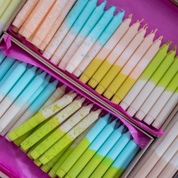 Assorted taper candles in earth-toned colors including shades of orange, yellow, green, and blue. The candles are arranged in a purple case, creating a vibrant and colorful display.