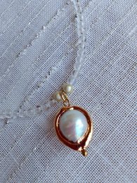 Transparent glass pendant necklace with a pearl-like bead in a gold-tone setting.