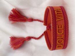 Colorful festival bracelet with tassels and text. Woven bracelet in red and orange with "Dolce Vita" text. Woven bracelet in gray with "Love Story" text.