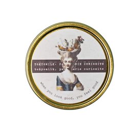  A round, white candle with a gold-colored lid and label. The label features an illustration of a deer or stag and the text "When You Look Good Stationery Candle".
