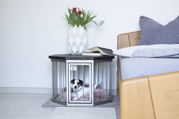 A small, hexagonal pet bed with a wooden frame and wire mesh sides, designed for a dog or cat. The bed has a gray cushion and is suitable for indoor use.