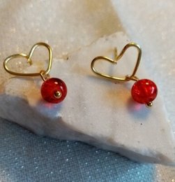 Gold heart-shaped stud earrings with red beads, perfect for adding a touch of romance to any outfit.