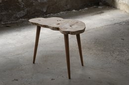 Wooden side table with natural wood grain and irregular shape, featuring tapered wooden legs.