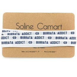 A pair of charm bracelets with the text "BURRATA ADDICT" printed on them. The bracelets appear to be made of leather or a similar material and have a simple, minimalist design.