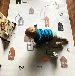 A large, rectangular natural rubber mat with a Scandinavian-inspired town design featuring various house-shaped illustrations in neutral tones.