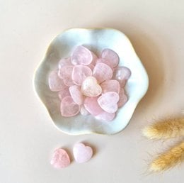  A collection of small, heart-shaped rose quartz stones in a white pouch. The stones have a soft, pastel pink color and a smooth, polished surface.