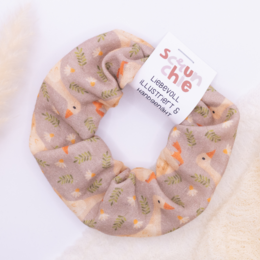 A hand-drawn and hand-sewn hair tie scrunchie featuring a meadow goose design in shades of brown, orange, and green.