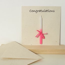  The product is a set of 2 greeting cards with a pink candle, handmade in eco-friendly paper in Nepal. The cards are labeled "Congratulations" and feature a pink ribbon tied in a bow. This product is suitable for baby-related celebrations or congratulatory occasions.