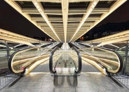 Escaliers enlumines is a painting featuring a symmetrical architectural interior with a grand staircase and ornate ceiling. The image showcases a striking, geometric design with a sense of grandeur and elegance.