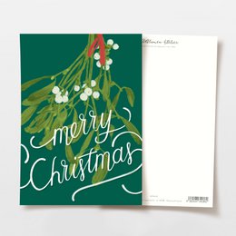 A postcard featuring a hand-drawn illustration of a deer with colorful antlers, surrounded by pine branches and pine cones. The text on the postcard reads "Merry Christmas" in a cursive font.