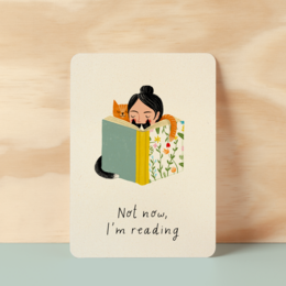 Postcard with text "Not now, I'm reading" and an illustration of a person reading a book.