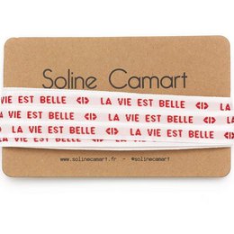 A pair of charm bracelet laces with the text "La vie est belle" (Life is beautiful) printed on them in a repeating pattern.