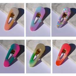 Colorful, geometric hair clips in various shapes and patterns. Includes clips in round, triangular, and abstract designs with vibrant color combinations.