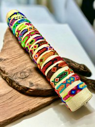  Colorful macrame woven bracelets in a variety of patterns and designs, including stripes, geometric shapes, and vibrant colors. The bracelets are presented on a wooden surface, showcasing their intricate textures and handcrafted nature.