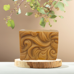 A handcrafted vegan soap bar with a swirling pattern in shades of brown and orange, accented with green leaves. The soap is presented on a wooden surface.