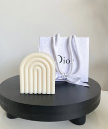 Tall, arched white candle with Dior branding. Made of wax material, suitable for home decor or gift-giving.