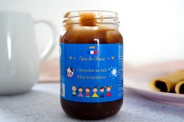 Creamy milk chocolate spread in a glass jar with a blue label featuring cartoon characters.