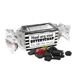 A rectangular candy box with a black and white striped design and the text "Heel erg veel beterschap" (Get well soon). The box contains various black and red hard candies.
