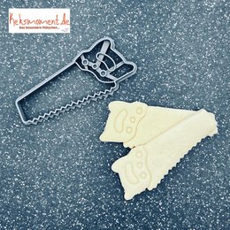 A black metal saw-shaped cookie cutter for baking and decorating. The saw-shaped cutter has a serrated edge and a handle, suitable for creating saw-shaped cookies or decorations.