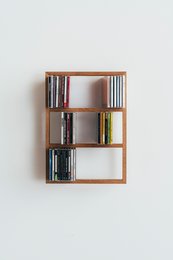 Wooden wall-mounted shelf unit with multiple compartments for storing CDs, books, and other items. Rectangular shape with a natural wood finish.