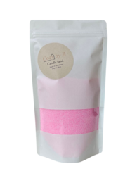 A tall, round pink candle in a glass container. The candle is labeled "Burning Sand Candle - Pink" and is categorized as a tealight.