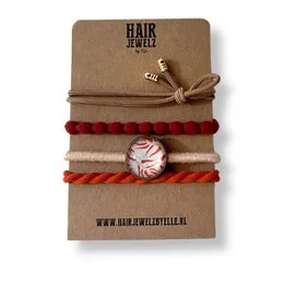 "Cognac Leaf headband with red and tan braided accents, featuring a metal charm."
The product is a headband made of a cognac-colored fabric with red and tan braided accents. It has a metal charm or pendant attached to it. The headband appears to be made of a soft, flexible material and is designed to be worn as a fashion accessory.