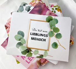 A white gift card with the text "Du bist mein Lieblingsmensch" (You are my favorite person) surrounded by green leaves and pink flowers.