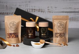 A gift box containing two jars of honey, a wooden spoon, and a decorative box. The honey jars feature a floral logo, suggesting a sweet and natural product. The overall presentation is elegant and gift-worthy.